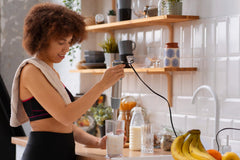 Woman preparing a protein shake by adding protein powder to a blender in a modern kitchen.