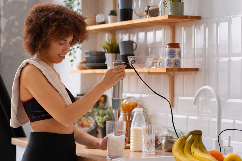 Woman preparing a protein shake by adding protein powder to a blender in a modern kitchen.