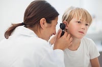 Doctor auscultating the ear of a child in examination room